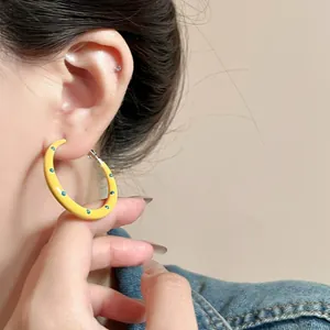Close-up detail of yellow enamel polka dot hoop earring worn by a model on a denim jacket