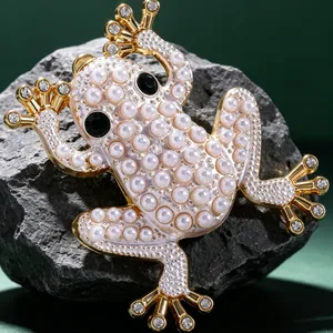 Exquisite goldene Froschbrosche mit weißen Perlen und Strasssteinen auf grauem Stein
