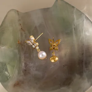 Vue détaillée de boucles d'oreilles papillon dorées avec pierres et perle pendante