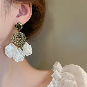Close-up of vintage gold hollowed-out earrings with black gemstone and white shell petals