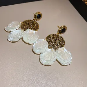 Close-up of vintage gold hollow discs and white petal pendants on elegant earrings