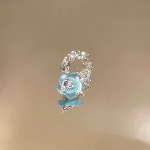 Nahaufnahme eines blauen Perlenblumenrings auf einer spiegelnden Goldfläche.
