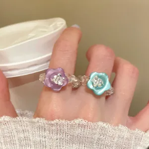 Nahaufnahme eines handgefertigten Perlenrings mit lila und türkisfarbenen Blumenanhängern.