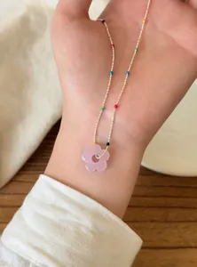 Detail einer bunten Perlenkette mit einem rosa Blumenanhänger an einer silbernen Kette.