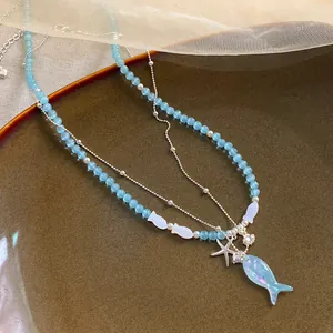 Detailed view of the iridescent blue fish pendant and beaded necklace layers.
