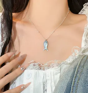 Detail of dainty blue fish pendant necklace with silver beaded chain on model's neck