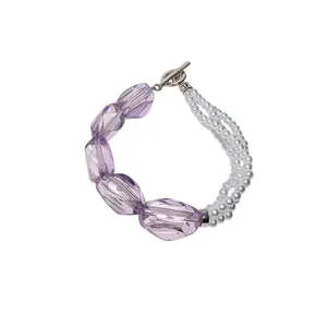 Elegante bracciale asimmetrico con perle in acrilico viola e perle bianche multistrato.