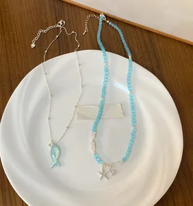 Detail of blue beaded necklace with starfish charm and iridescent fish pendant on a white plate