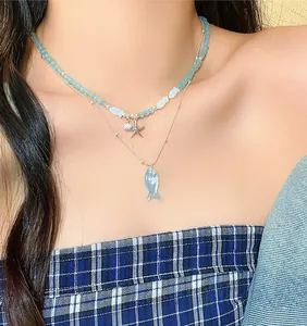 Close-up of a layered blue beaded fish necklace and silver chain on a model's neck