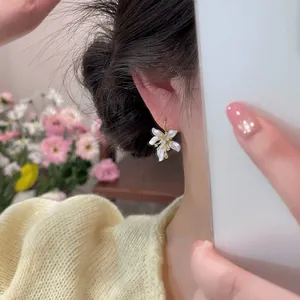 Detail view of a dainty white flower earring worn on the ear against a soft background.