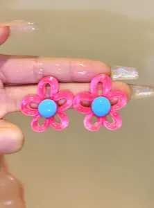Detailed view of pink and blue flower stud earrings held in hand for scale and texture