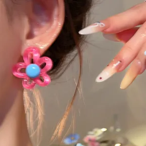 Detail of pink and blue dopamine flower stud earring on ear with manicured nails