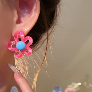 Detailed close-up of a vibrant pink and blue flower stud earring worn on ear.