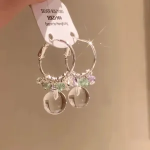 Macro detail of forest style crystal bead hoop earrings with clear spherical pendants