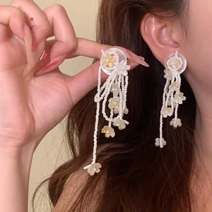 Detailed macro view of long white beaded tassel earrings with yellow flower charms on ear