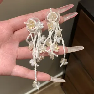 Macro detail view of white beaded tassel earrings featuring delicate flower charms