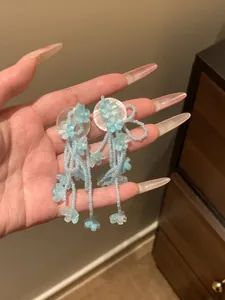 Detailed view of light blue beaded tassel earrings with flower charms held in hand