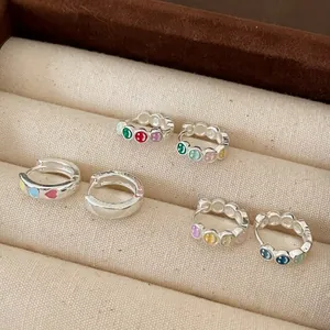 Detail view of silver hoop earrings with colorful smiley and heart enamel patterns