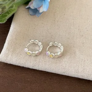 Close-up of silver hoop earrings with vibrant colorful smiley face enamel charms.