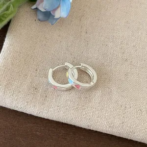 Close-up detail of silver hoop earrings featuring colorful enamel heart patterns.