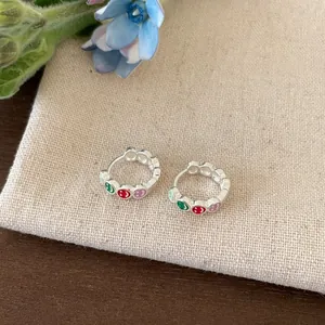Close-up of silver earrings with colorful enamel smiley faces on a textured pouch