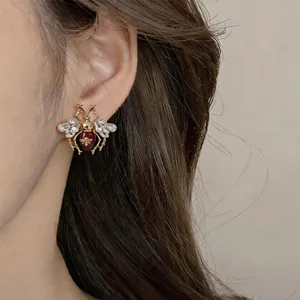 Close-up of vintage insect stud earring with red enamel and crystals on model ear