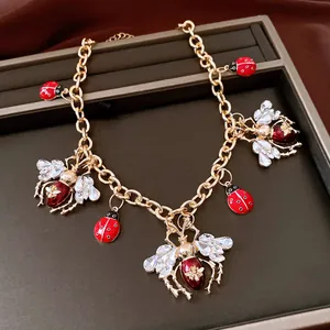 Gold-plated insect charm necklace featuring crystal bees and red ladybugs on a jewelry tray.