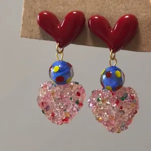 Close-up view of heart drop earrings featuring red resin hearts and pink crystals