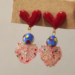 Macro detail of colorful resin heart drop earrings with glitter bead embellishments