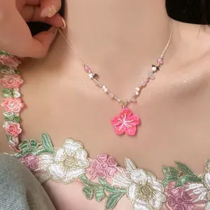Detailed view of a beaded necklace featuring a vibrant pink flower pendant on a model's neck.