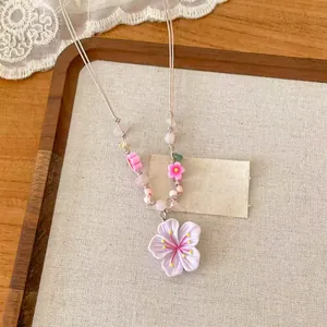 Vue détaillée montrant le pendentif fleur violette et le cordon perlé rose sur texture
