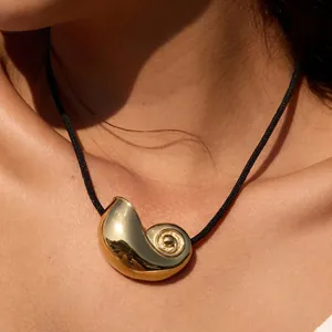 Close-up view of a minimalist golden spiral pendant on a black cord necklace worn by a model