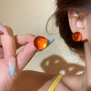 Close-up detail of vibrant orange translucent sphere stud earrings on model's ear