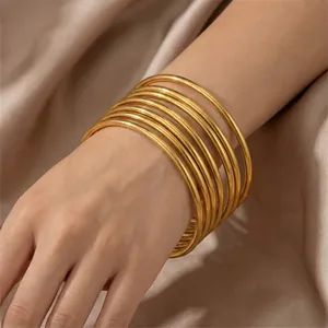 Detailed view of multiple 3mm stackable 18k gold plated stainless steel bangles on wrist