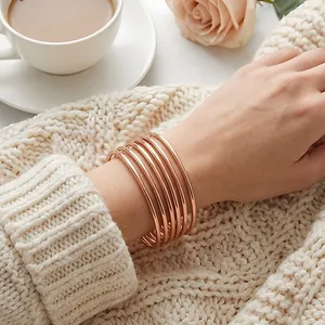 Close-up of polished rose gold stackable 3mm stainless steel bangles worn over a knit sweater