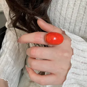 Close-up of a vibrant orange oval resin ring worn on a finger, minimalist style.