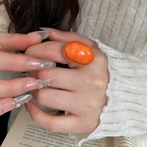 Close-up of a large orange oval resin ring worn on a hand, highlighting its glossy finish.