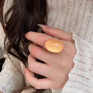 Close-up of a minimalist peach resin oval ring worn on index finger