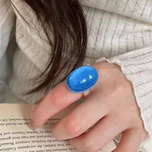 Close-up detail shot of a vibrant blue resin oval ring worn on the finger in a lifestyle setting