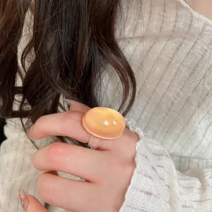 Close-up of a large oval amber orange resin ring with smooth translucent texture.