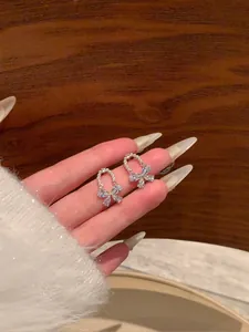 Detailed view of sparkling diamond bow earrings with pearls held to show size and luster