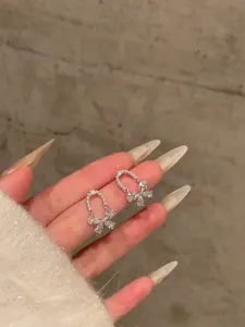 Close-up detail of sparkling bow earrings with shimmering rhinestones and pearls on a hand.