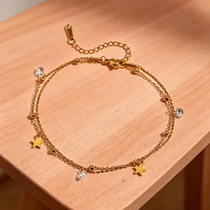 Close-up of double-layered gold anklet with star charms and crystals on a wooden surface
