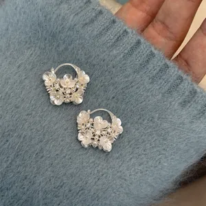 Detailed view of silver floral basket earrings with pearls and rhinestones on blue fabric.