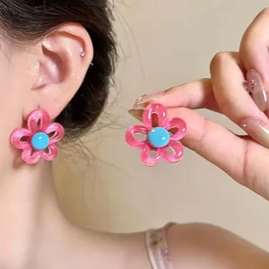 Vue détaillée des boucles d'oreilles fleur évidée rose avec perle bleue centrale