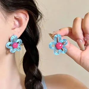 Détail boucles d'oreilles fleur bleue évidée avec centre rose sur oreille et main