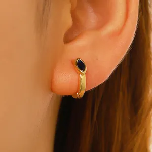 Close-up of golden huggie hoop earring featuring a marquise-cut navy blue stone charm