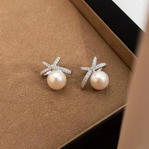 Elegant white pearl earrings with a sparkling cross design on luxury jewelry display