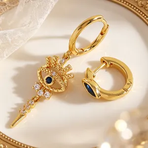 Detail of asymmetric gold evil eye hoop earrings with blue stones and white crystals