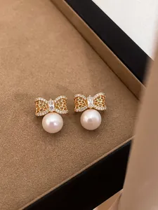 Elegant close-up of golden bow-knot stud earrings featuring white pearls and crystals